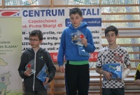 Trzech chłopaków stojących na podium trzymających nagrody